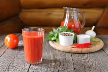 A tasty tomato juice in a glassware and fresh tomatoes with vegetables, herb and seasoning are on a wooden background.  