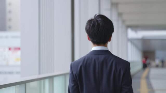 スーツを着て歩く若い日本人ビジネスマンの後ろ姿のスローモーションイメージ
