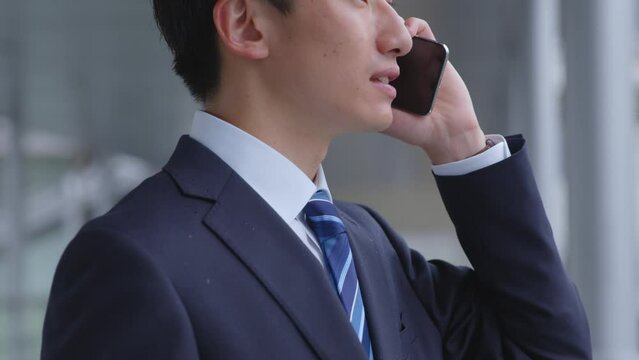 駅にてスマートフォンを使用して仕事をするスーツを着た若い日本人ビジネスマン