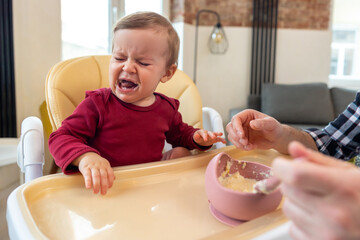 Infant little baby girl crying and don't want to eat food from her father. - obrazy, fototapety, plakaty