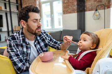 Father teaching his little baby to eat porridge from spoon infant daughter.