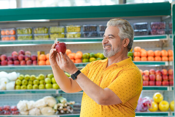 Senior indian man showing apple fruit at fruit shop. Healthy lifestyle concept.