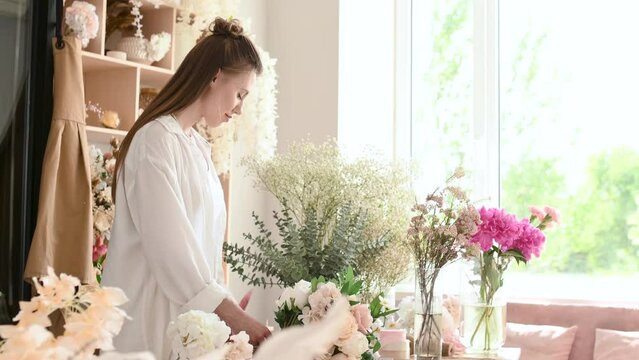 A woman florist is working hard in a flower shop. Floral design studio, making decorations and arrangements. Flower delivery, order creation. Small business.