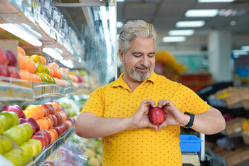 Senior indian man showing apple fruit at fruit shop. Healthy lifestyle concept.