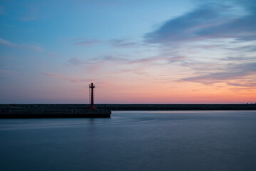 The lighthouse at harbor with clouds in golden hour.The quite beautiful orange tone sunset at Tainan quigu of Taiwan.The sky had fantastic hue and the sea looks quite peaceful.It's long exposure photo
