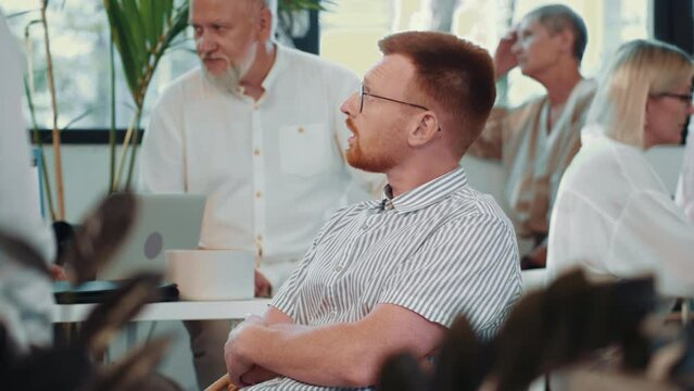 Bored young Caucasian employee catching flies at team meeting in busy office