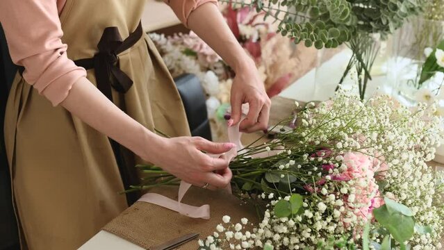 Woman florist makes a bouquet at home in the decoration studio. female hands close-up tying a silk ribbon on a bouquet. Closeup. no face top view