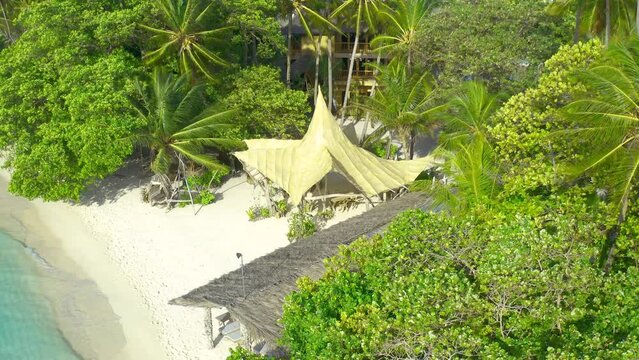 Aerial top view on white sand beach with thatched huts and lush tropical island Bora Bora, French Polynesia.