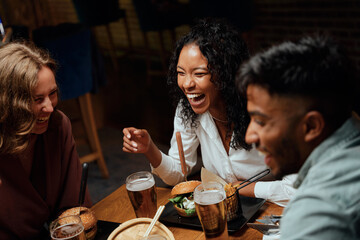 Happy young multiracial group of friends in casual clothing laughing during conversation over dinner