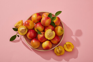 Flat lay of a dish in pink color containing many peaches, a peach cut in half placed on the background. Eat Peach (Prunus persica) for an antioxidant boost