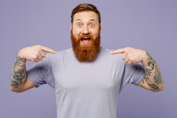 Young overjoyed excited redhead bearded man wear violet t-shirt casual clothes pointing index...