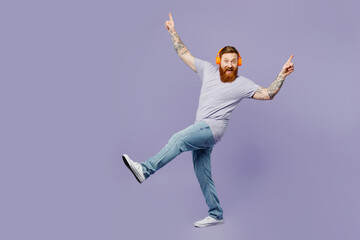 Full body young redhead bearded man he wearing violet t-shirt casual clothes headphones listen to...