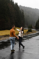 Obraz premium a couple of lovers run along a mountain road overlooking the forest. a man and a woman have a fun trip running in the rain on a high road. autumn time.