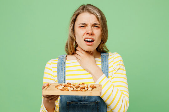 Sick unhealthy ill allergic woman has red watery eyes runny stuffy sore nose suffer from allergy trigger symptoms hay fever hold neck peanuts nuts isolated on plain green background studio portrait.