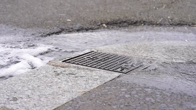 4K Footage of Water Pouring from Manhole in Roadside Drain. Water pours out of a manhole and flows through the roadside drain, revealing the interplay between urbanization and the natural phenomenon.