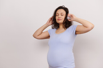 Multi ethnic brunette, happy adult pregnant woman listening to soothing music on wireless...