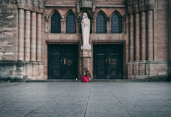 Lone homeless woman with red blanket sitting at the steps of Cathédrale Notre-Dame. Feeling of...