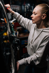 Naklejka na ściany i meble Vertical side view of focused cycling mechanic female repairing and fixing mountain bicycle standing on bike rack in repair workshop with dark interior. Concept of professional bicycle maintenance.