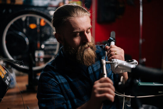 Closeup portrait of concentrated cycling mechanic male checking and repairing bicycle handlebar with special tools working in bike repair shop with dark interior. Concept of maintenance of bike.