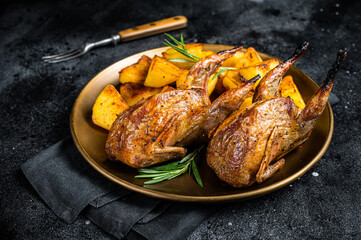 Delicious roasted quails with herbs in a plate with fried potato. Black background. Top view