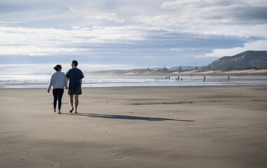 Naklejka premium Young couple holding hands and walking barefoot on Muriwai beach. Auckland.