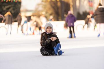 A girl fell at the ice rink in winter. the girl sits on the ice in skates, after a fall.