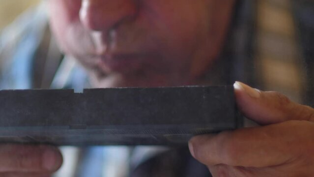close-up of an elderly man blowing dust from an old video cassette, slow motion. selective focus. old home video archives. vintage video cassette in the dust