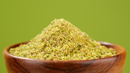 Pistachio flour in wooden bowl, green background. Ground pistachio ingredient for dessert and...