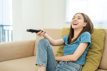 Happy Young asian woman watching television using remote to change the program menu. Very enjoy and...