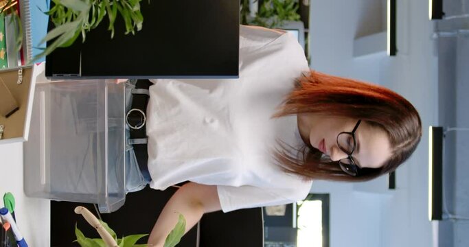 Vertical shoot. Office worker with sadness on face collects stuff. Girl was fired from company. Employee collects stationery in box from desktop. Female feel pity saying goodbye to position.