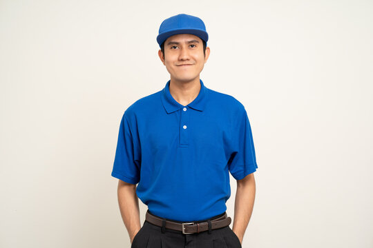 Happy asian man in blue uniform standing on isolated white background. Smiling male delivery service worker. Delivery courier and shipping service.