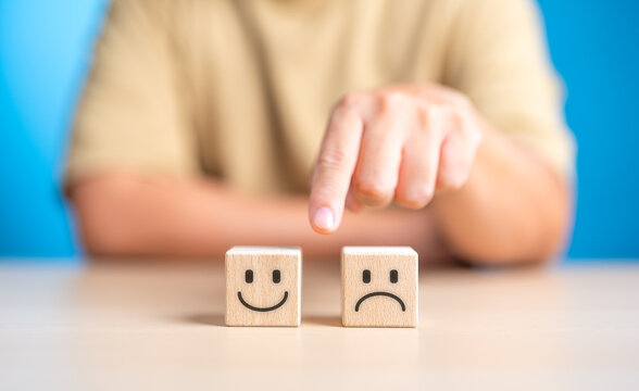 Hand making a decision between two wooden cubes with happy and sad face for positive or negative mindset selection. Emotional state and mental health concept. Like or Dislike for client satisfaction.