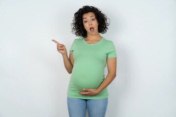 Emotive Beautiful pregnant woman wearing green T-shirt standing keeps jaw dropped from shock...