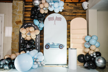 Trendy decor with flag, race, wheel, car for boy. Birthday decorations with blue, brown, black, silver balloons for party. Arch for a celebration event. Photo wall decoration space or place for text.