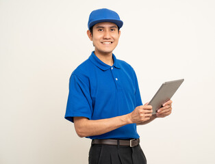 Asian man in blue uniform standing holding digital tablet computer on isolated white background. Male service worker with cell phone. Delivery courier shipping service