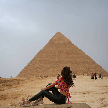 Beautiful brunette girl sitting in front of and looking at the Pyramid of Giza