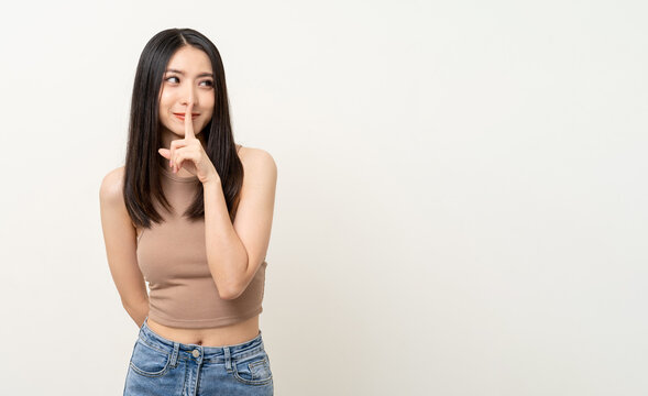 Happy Beautiful Asian Woman Whispering Some Secret Gossip. Excited Pretty Girl Index Finger On Mouth Standing Pose On Isolated White Background.