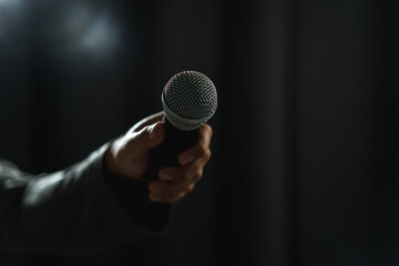 Confident successful speaker man talking on stage with spotlight strike through the darkness at...