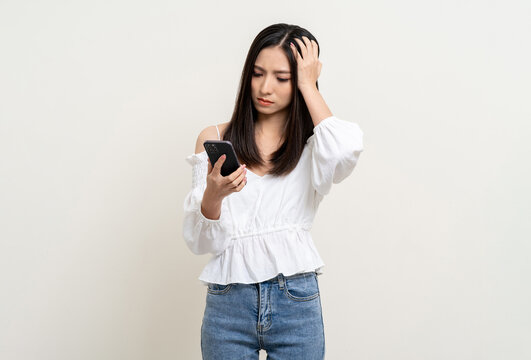 Pretty young asian woman using smartphone feeling upset confused bad depressed emotional standing on isolated white background. Holding cell phone. Thinking and stressed