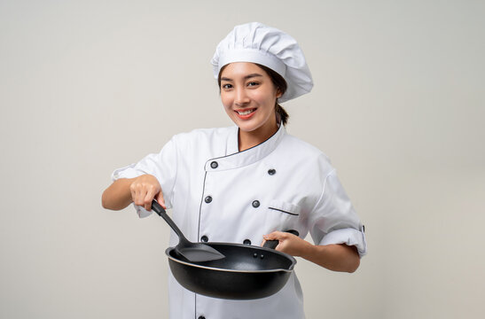 Young beautiful asian woman chef in uniform holding turner and iron Frying pan utensils cooking in the kitchen various gesture on isolated background. woman occupation chef restaurant and hotel.
