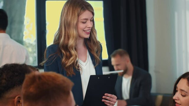 Professional young female manager pitching project idea to clients during meeting in busy modern office