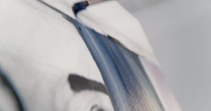 Close-up of the artist's brush painting on canvas, stroking up and down with blue paint. Camera follows movement.