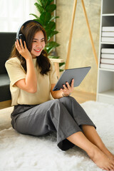 Happy young woman wearing headphones, using digital tablet in living room, listening to music, watching video, podcast