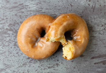 Top view of a bitten and whole freshly baked cake donut on a gray mottled countertop.