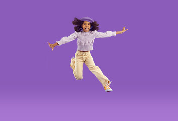 Hooray. Happy joyful kid girl in comfortable trendy wear jumping high. Full length portrait African child with curly hair, in funky pants and beret hat feeling free, overjoyed, excited and having fun