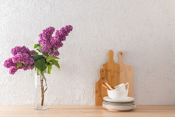 Beautiful kitchen background in a minimalist style. A modern glass vase with a lilac branch and a set of cutting boards with bowls. gray wall.