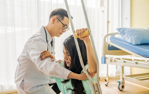 Front View Of Asian Male Doctor Helping Female Patient To Walk Out The Hospital Bed, Medicine And Health Care Concept, Selective Focus Point