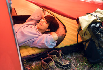 ソロキャンプをしている若い日本人女性/テントの中で寝転んでいる