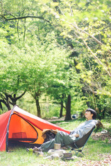 ソロキャンプをしている若い日本人女性/椅子に座りくつろいでいる