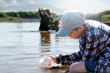 Asian boy is collecting river water samples in transparent containers to measure and monitor water...